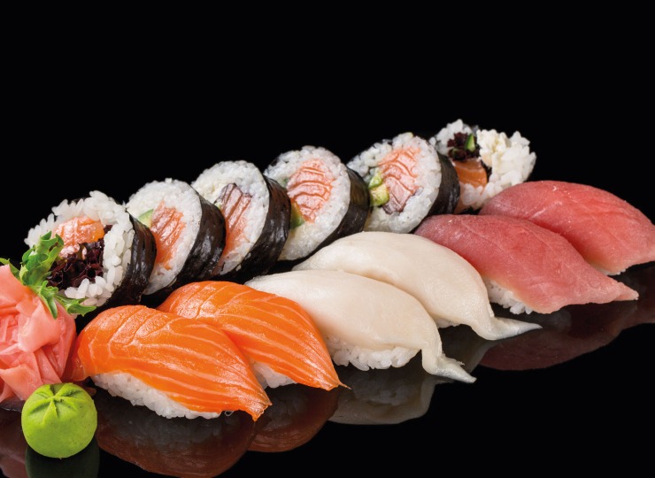 A selection of sushi arranged with wasabi and garnish on a shiny black surface